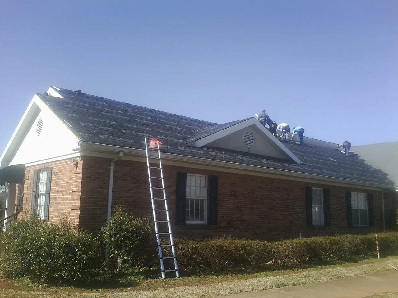 Crew tearing shingles off a brick ranch roof with a ladder set — Emergency Roof Repair work by our crew in New Hartford