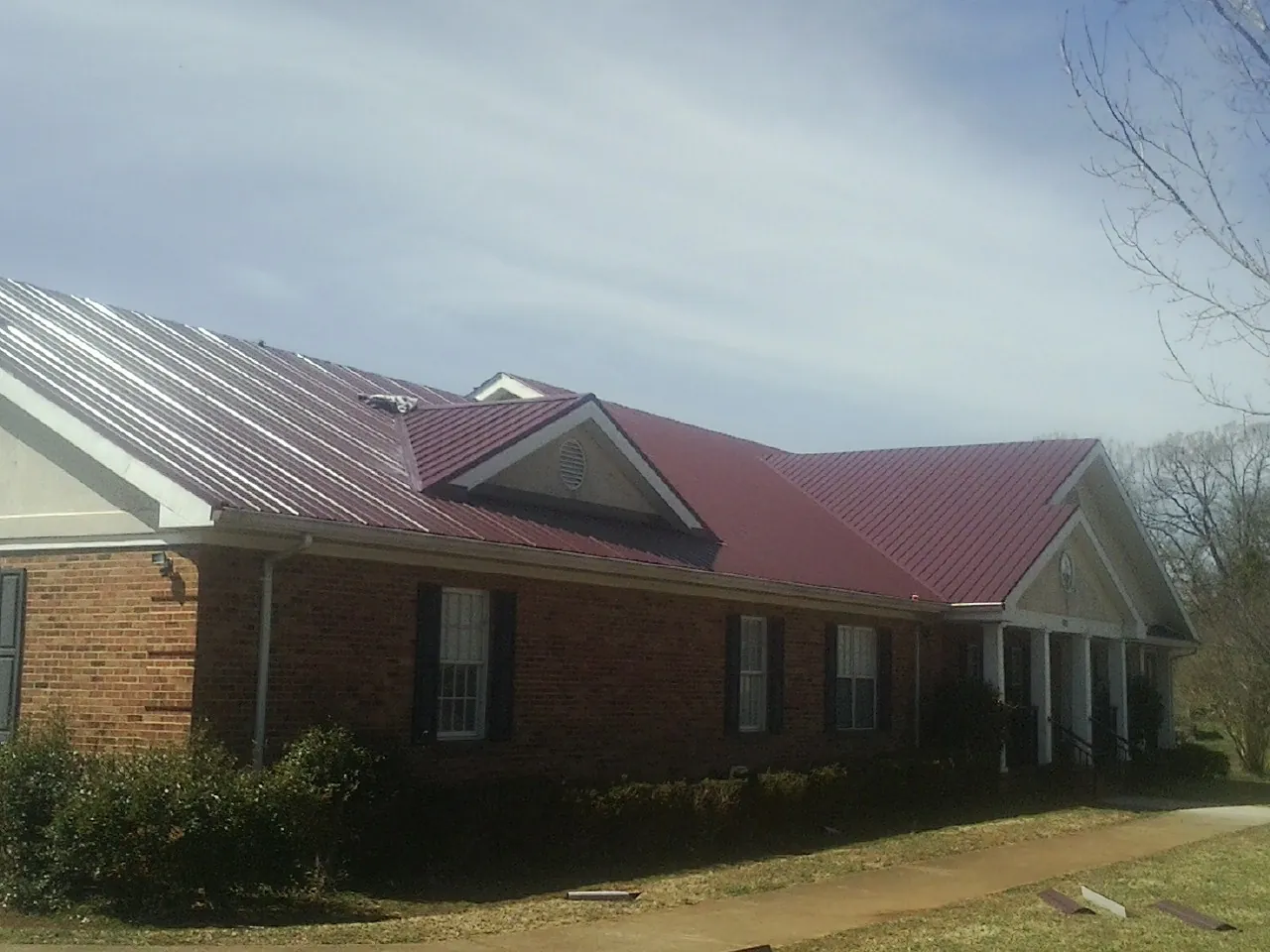 Red metal roof with gabled entries on a long brick building, from a Hail Damage Roof Repair job in New Hartford