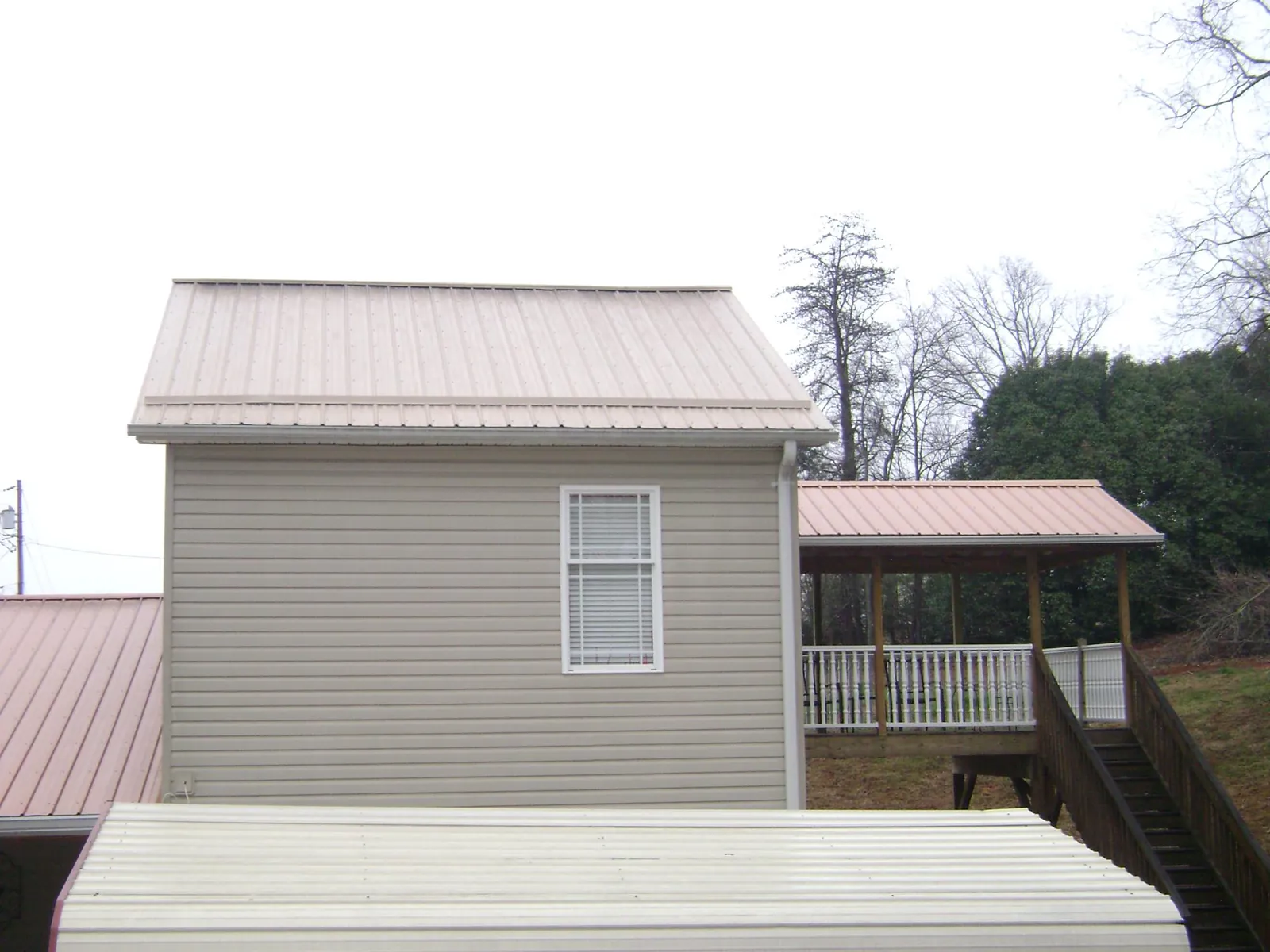 Tan metal roofs on a two story addition and attached porch, from a Roof Replacement job in New Hartford